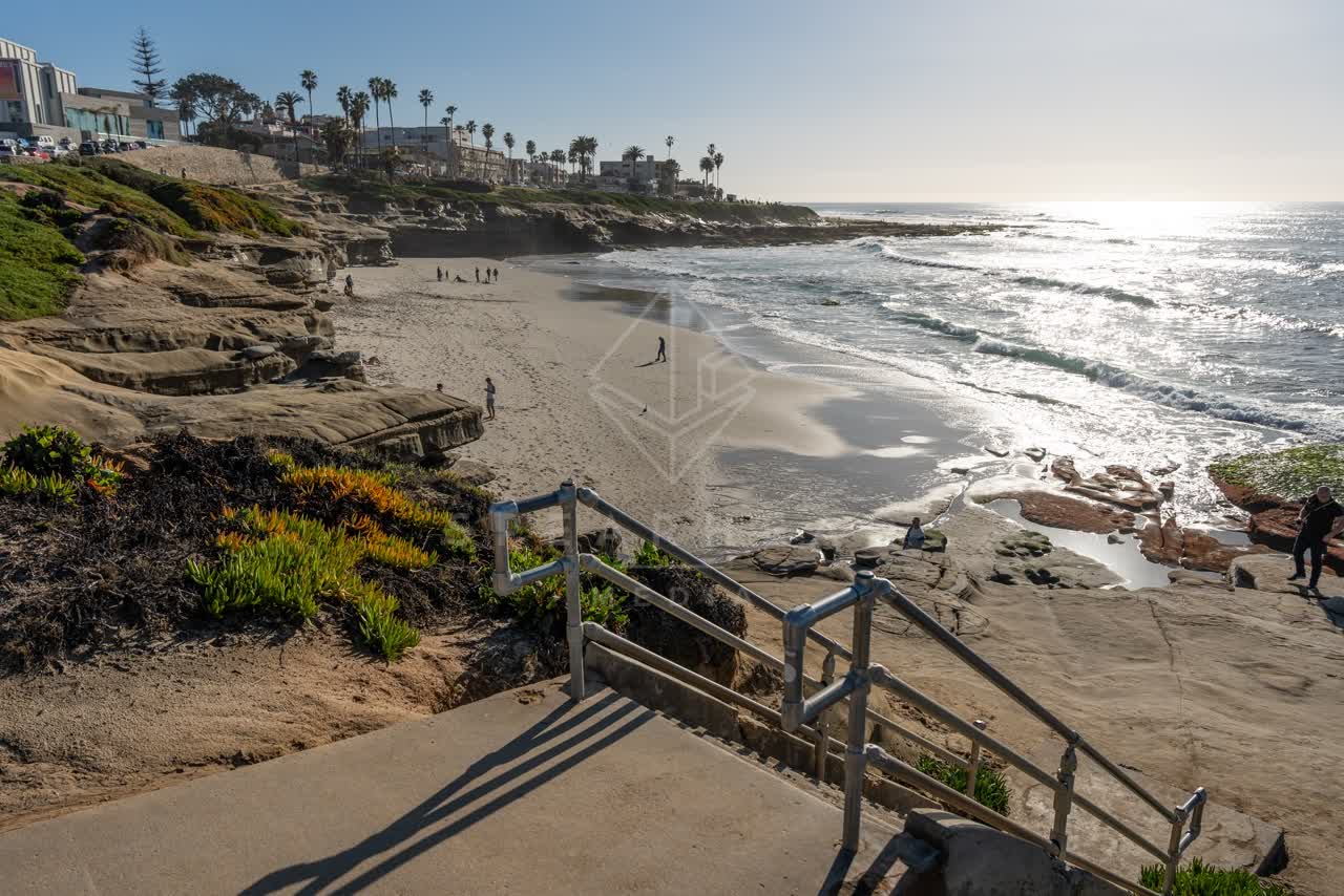 Elevated view of the beach, the surf and palm trees at La Jolla Cove, with people walking.