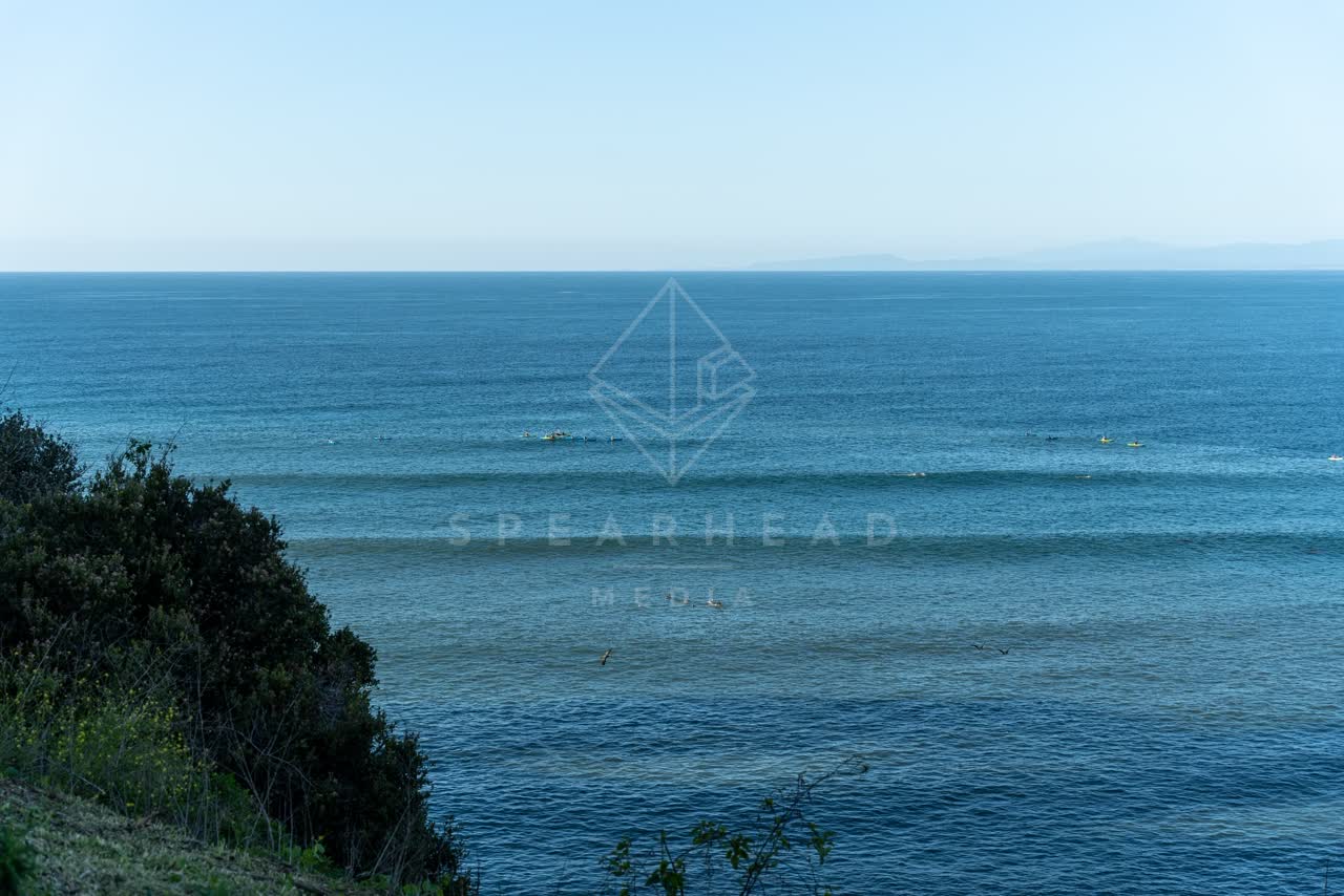 Elevated view of the cliffs, the surf and the ocean at Coast Walk Trail, with surfers out.
