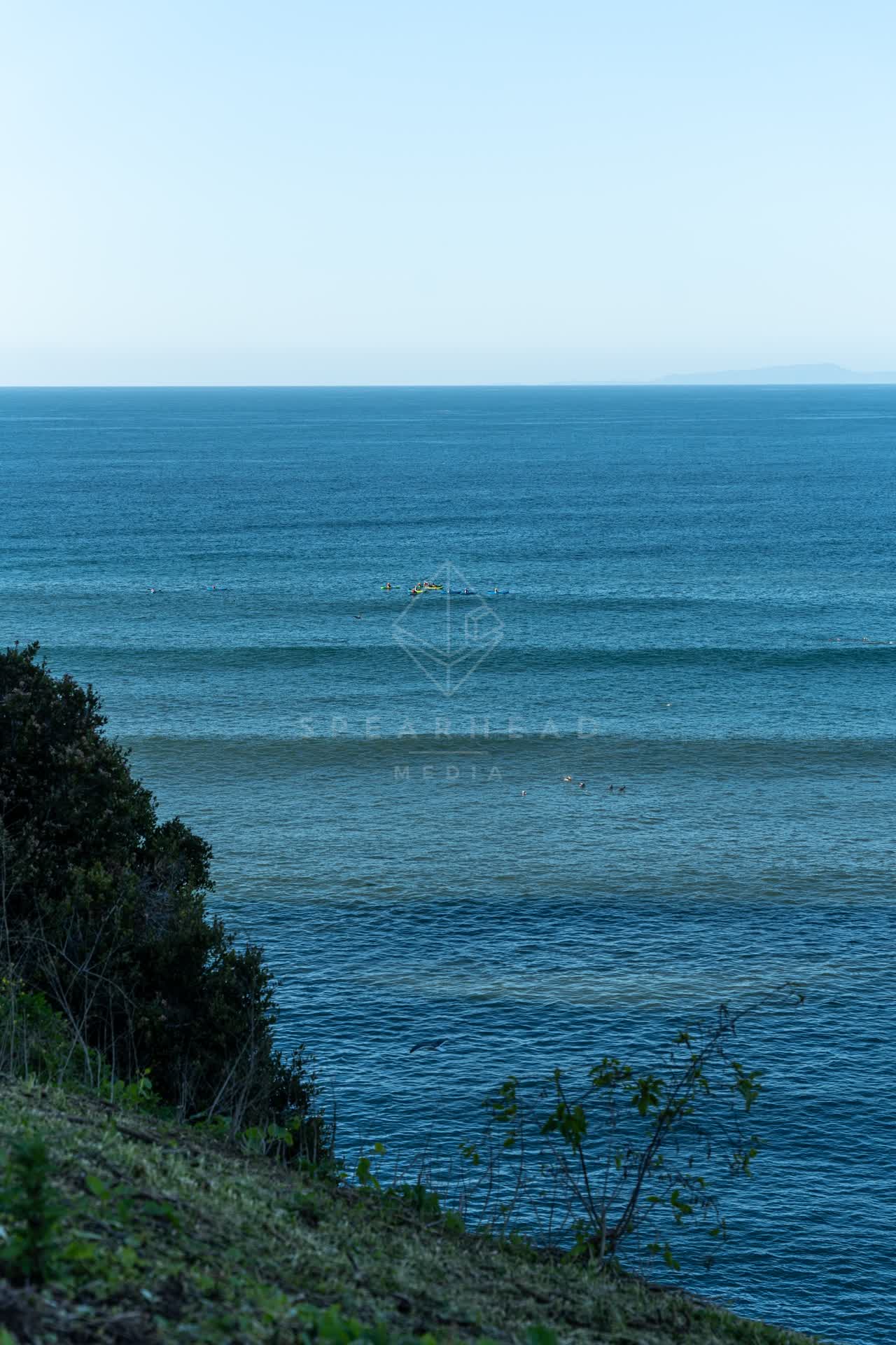 Elevated view of the cliffs, the surf and the ocean at Coast Walk Trail, with surfers out.