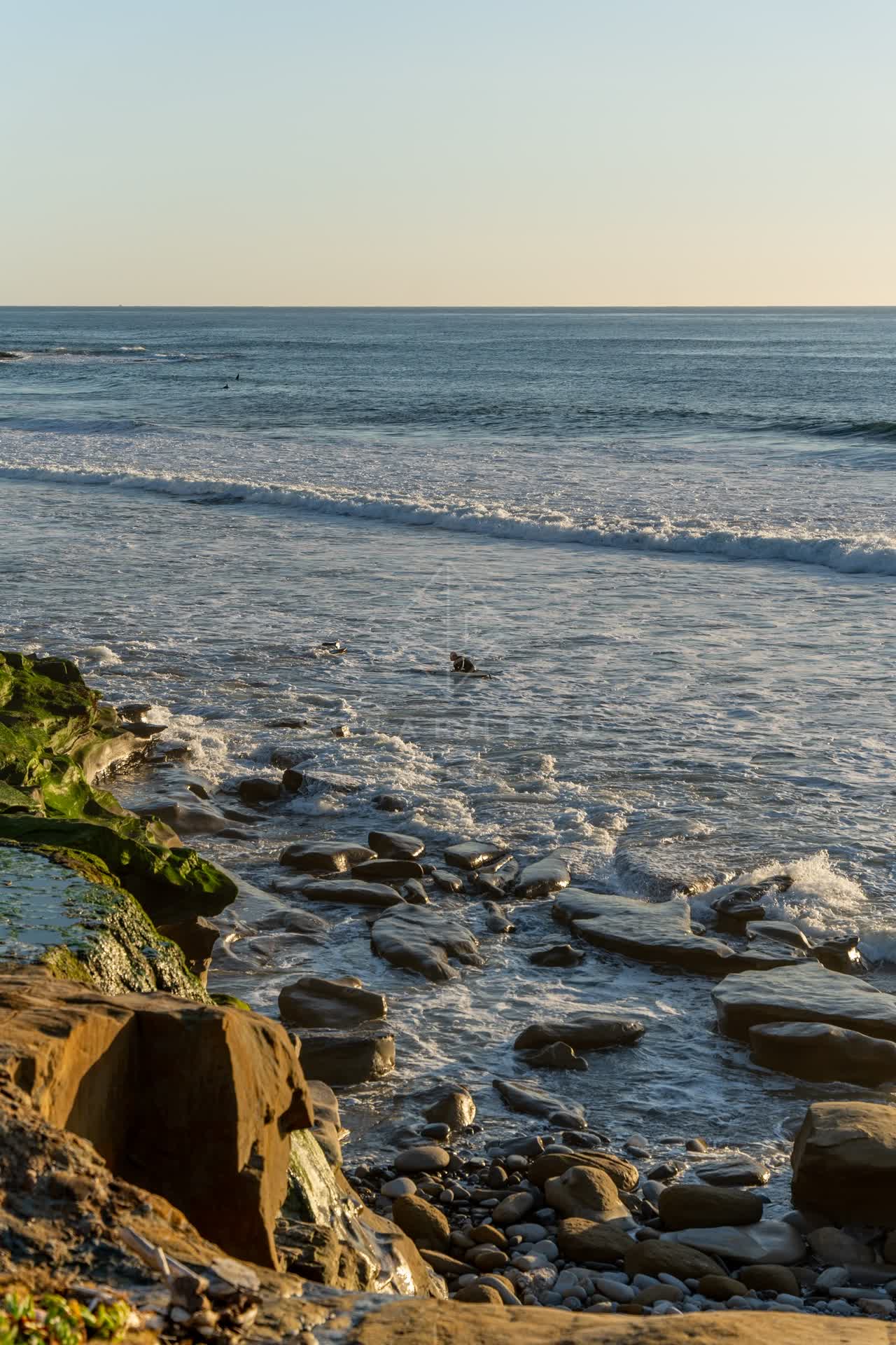 Elevated view of the cliffs, the surf and the ocean at Windansea, with surfers out.