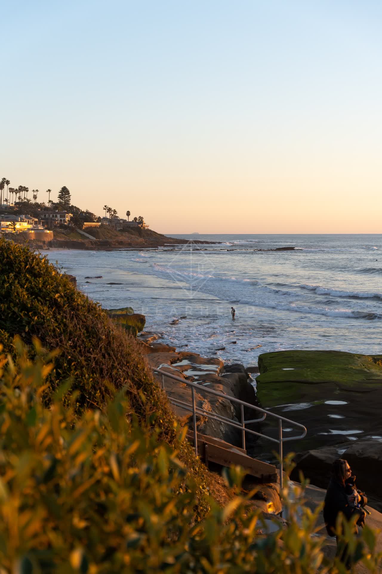 Elevated view of the cliffs, palm trees and the ocean at Windansea, with people walking.