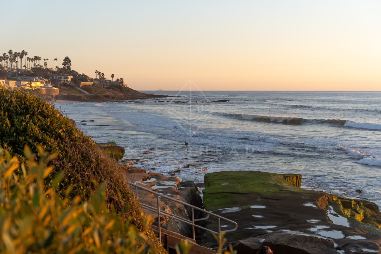Elevated view of the cliffs, the surf and palm trees at Windansea, with people walking.