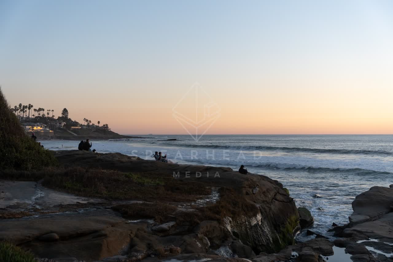 Elevated view of the cliffs, the surf and palm trees at Windansea, with a crowd gathered.