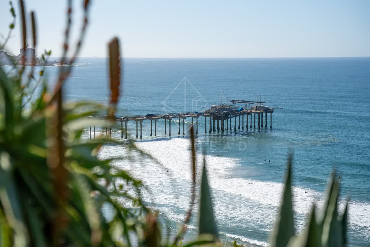 Elevated view of the cliffs, the surf and the pier at La Jolla Shores, with surfers out.