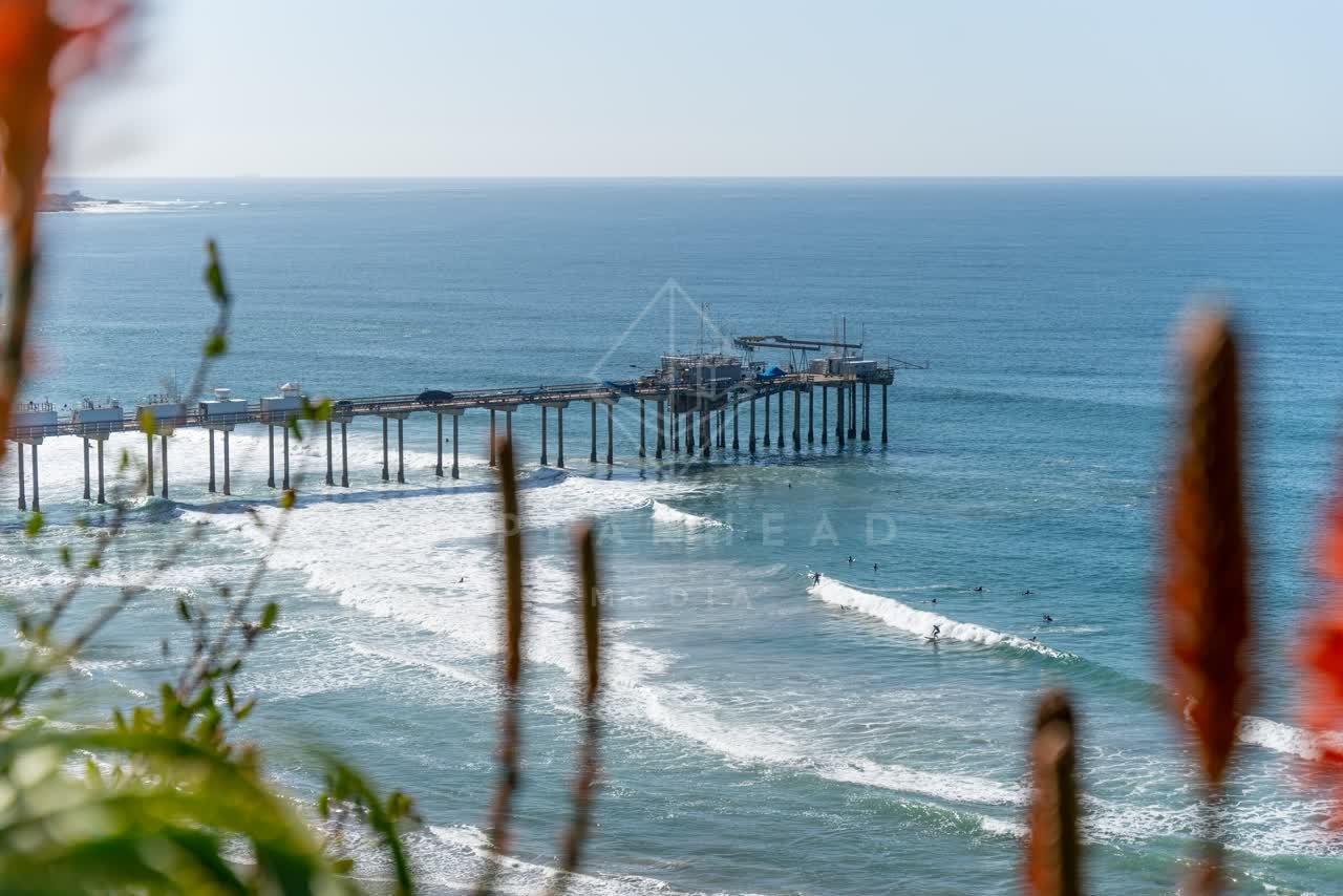 Elevated view of the cliffs, the surf and the pier at La Jolla Shores, with surfers out.
