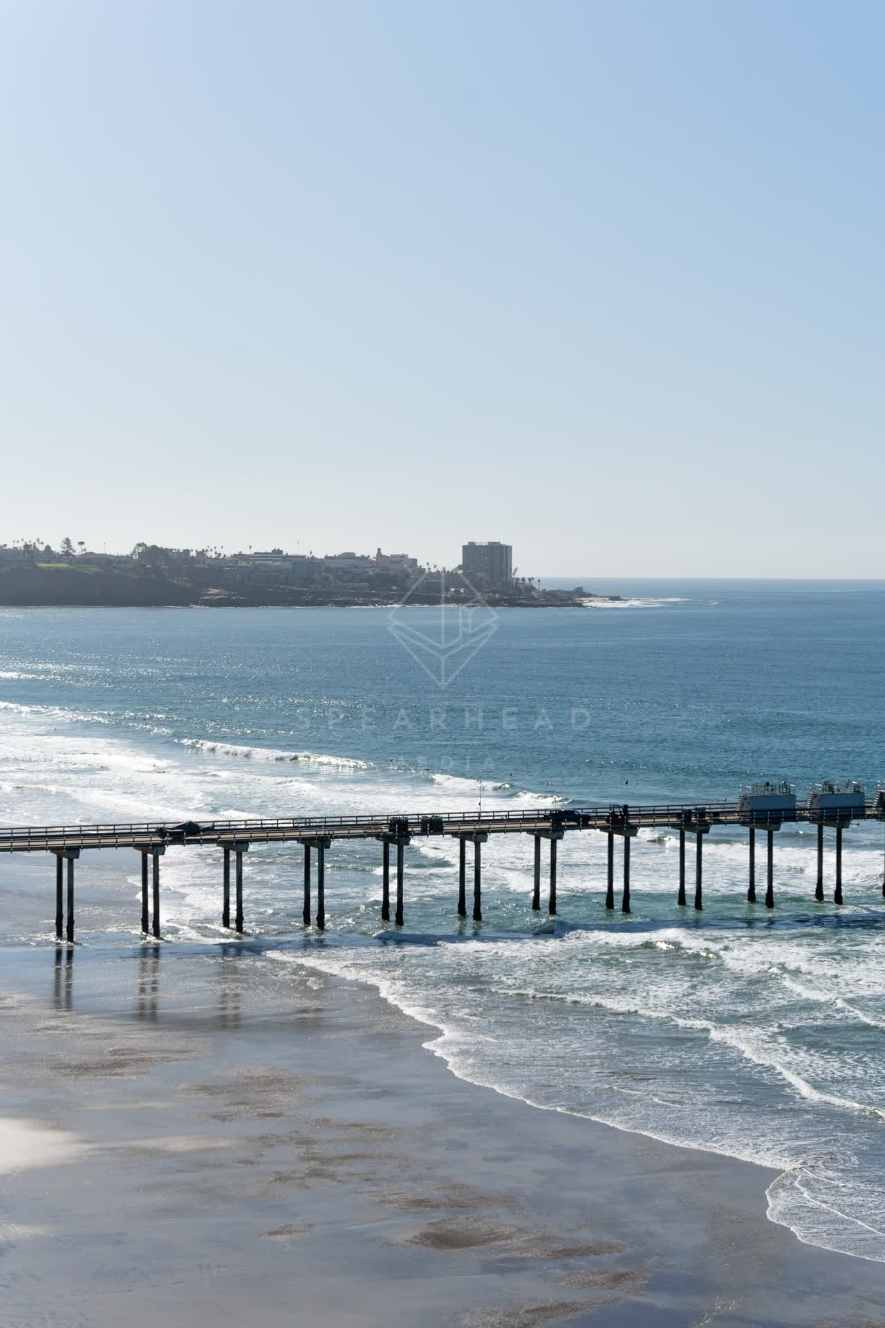 Elevated view of the beach, the surf and the pier at La Jolla Shores, with people walking.