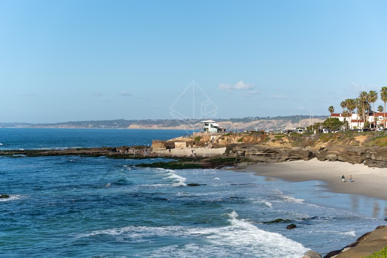 Elevated view of the cliffs, the surf and palm trees at La Jolla Cove, with people walking.