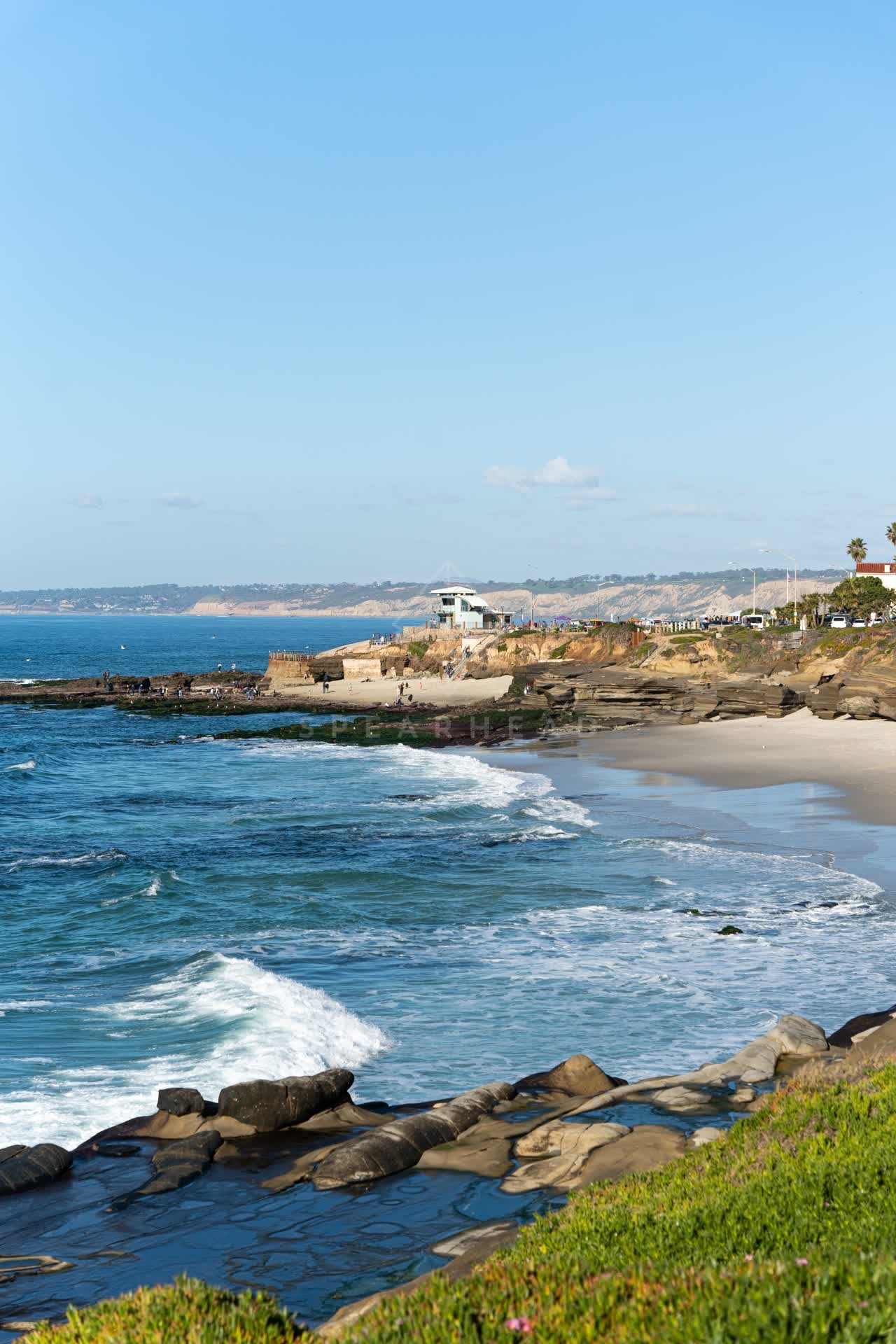 Elevated view of the beach, the surf and palm trees at La Jolla Cove, with people walking.