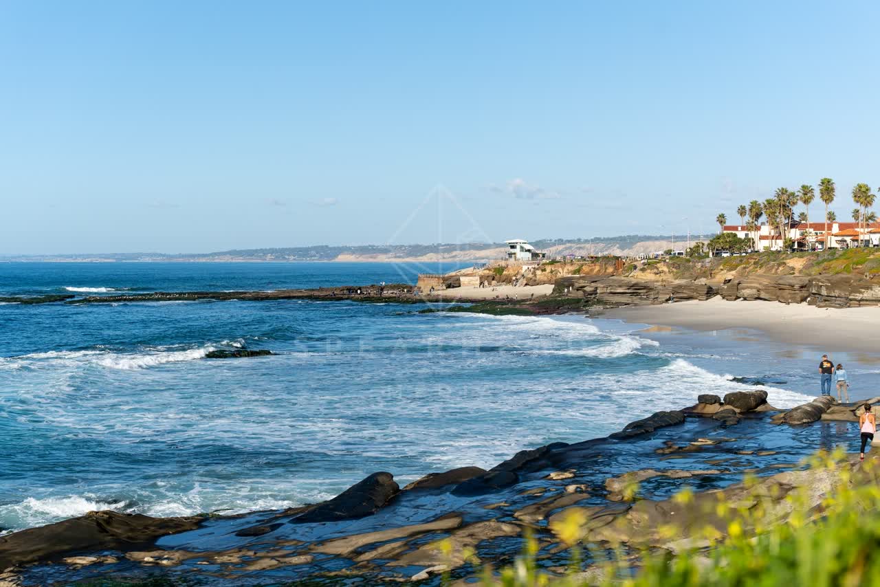Elevated view of the beach, the surf and palm trees at La Jolla Cove, with people walking.