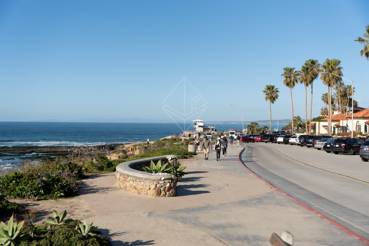 Elevated view of the beach, palm trees and the ocean at La Jolla Cove, with people walking.