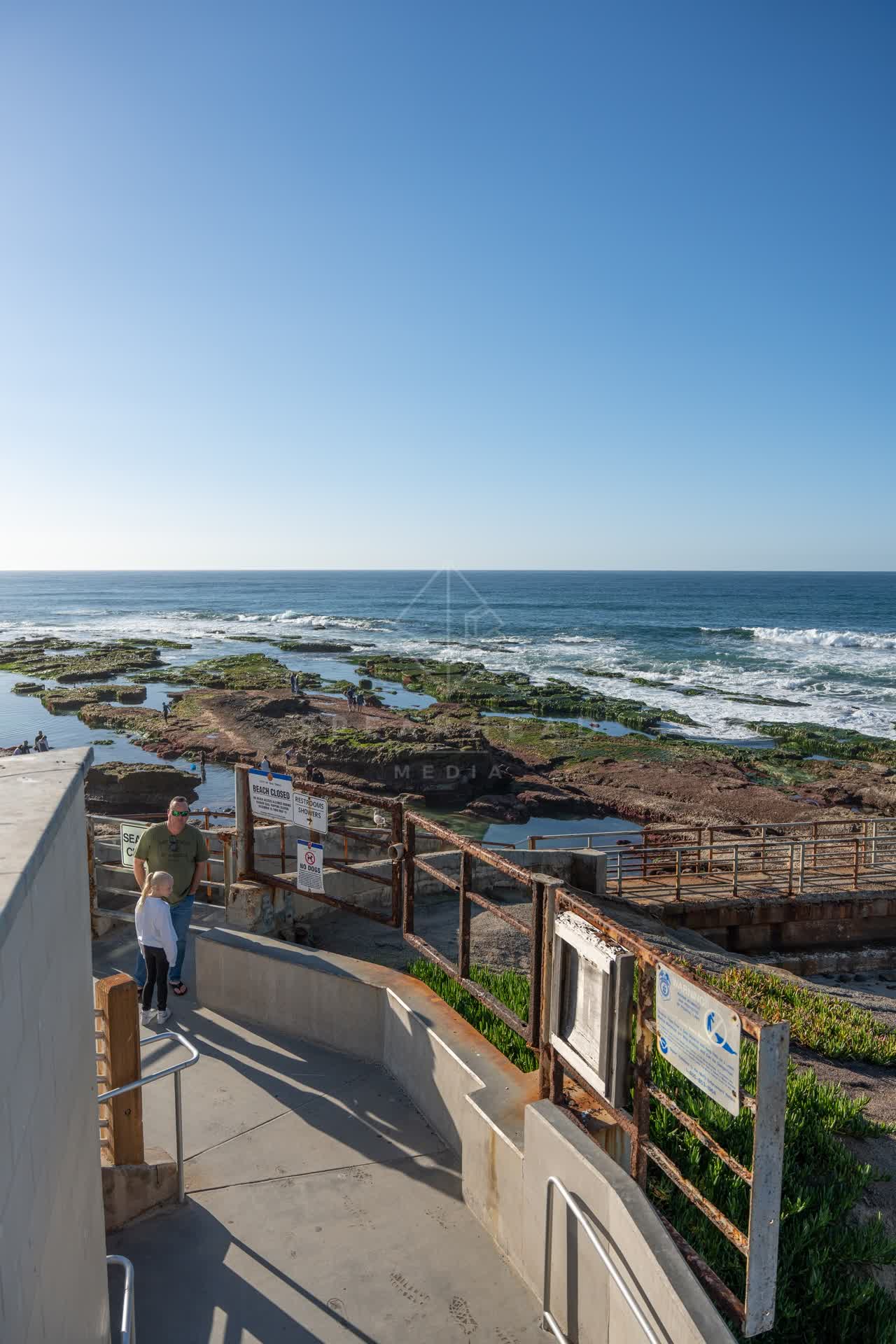 Elevated view of the cliffs, the ocean and open country at La Jolla Cove, with people walking.