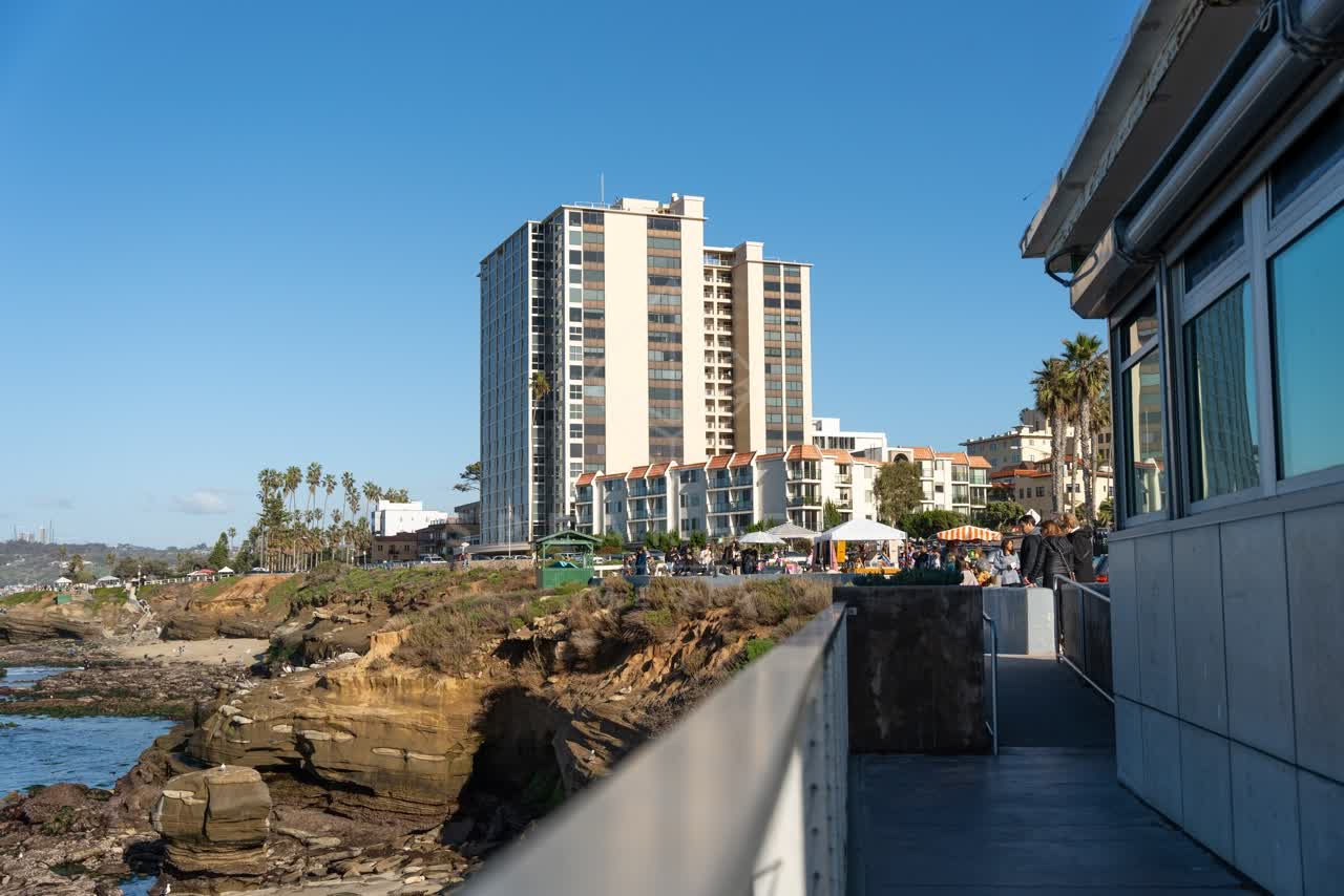 Elevated view of the cliffs, palm trees and the ocean at La Jolla Cove, with a crowd gathered.