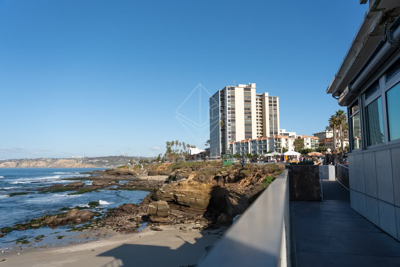 Elevated view of the cliffs, palm trees and the ocean at La Jolla Cove, with people walking.
