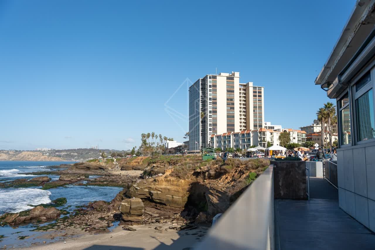Elevated view of the cliffs, palm trees and the ocean at La Jolla Cove, with a crowd gathered.