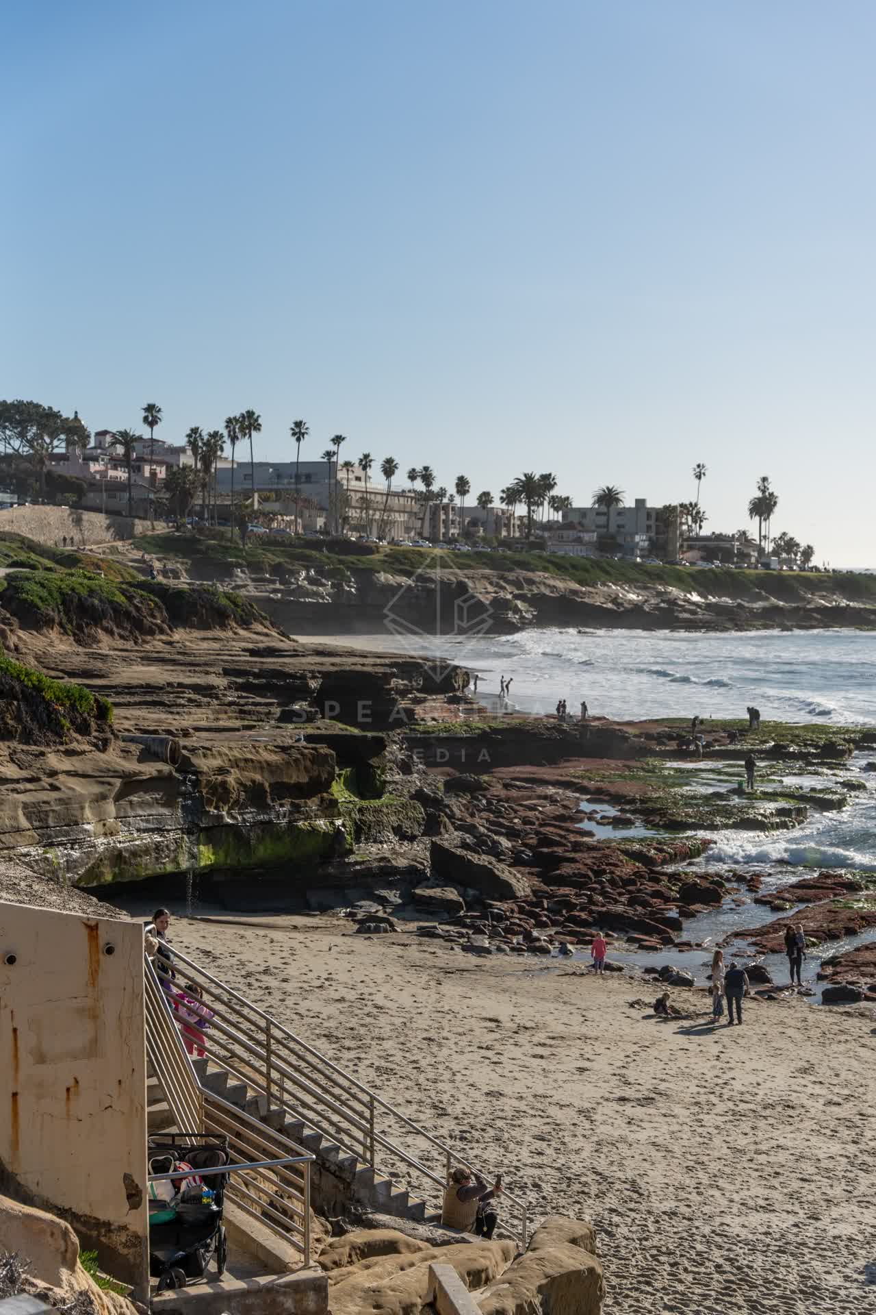 Elevated view of the beach, the surf and palm trees at La Jolla Cove, with people walking.