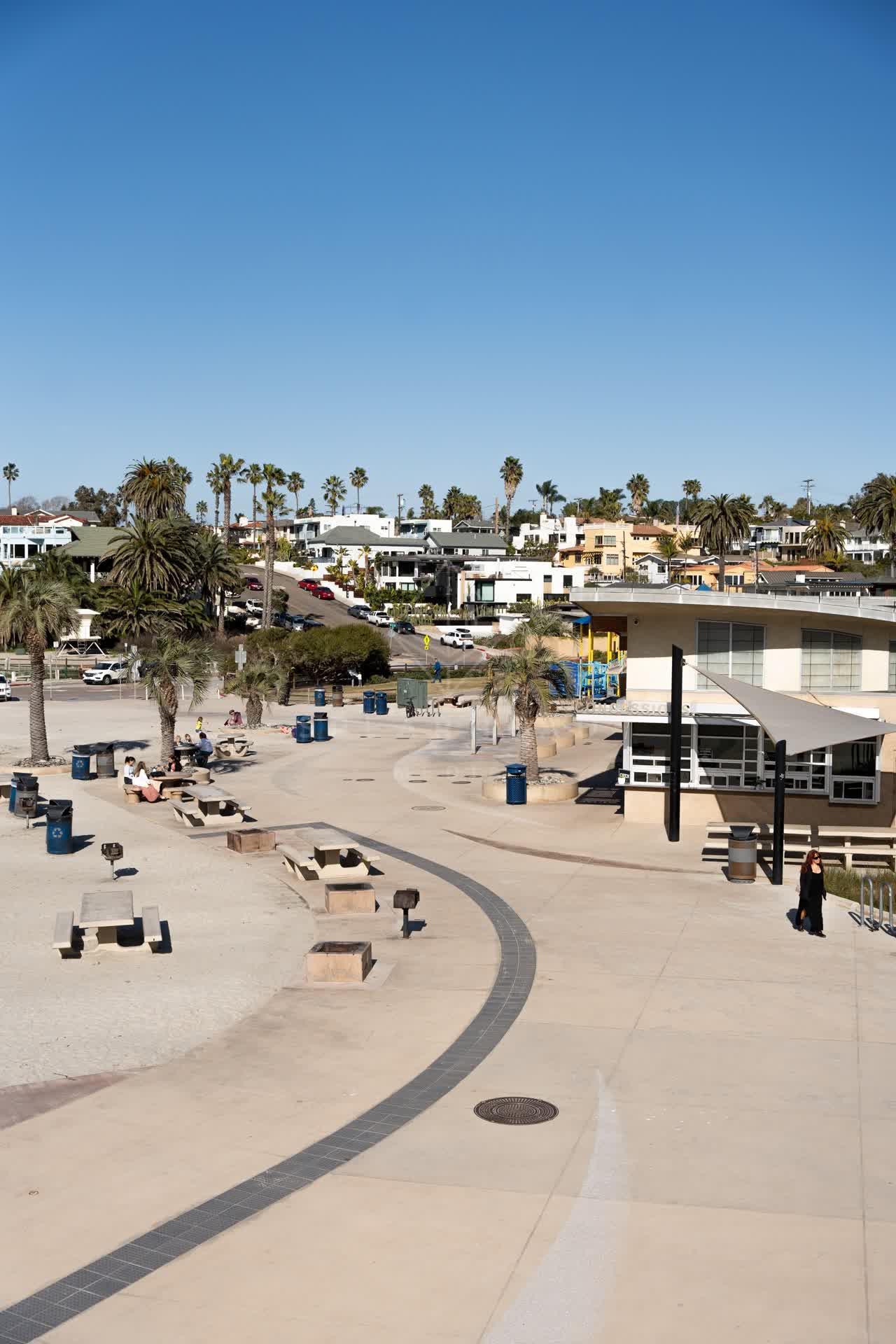 Elevated view of the beach, palm trees and homes at Moonlight Beach, with people walking.