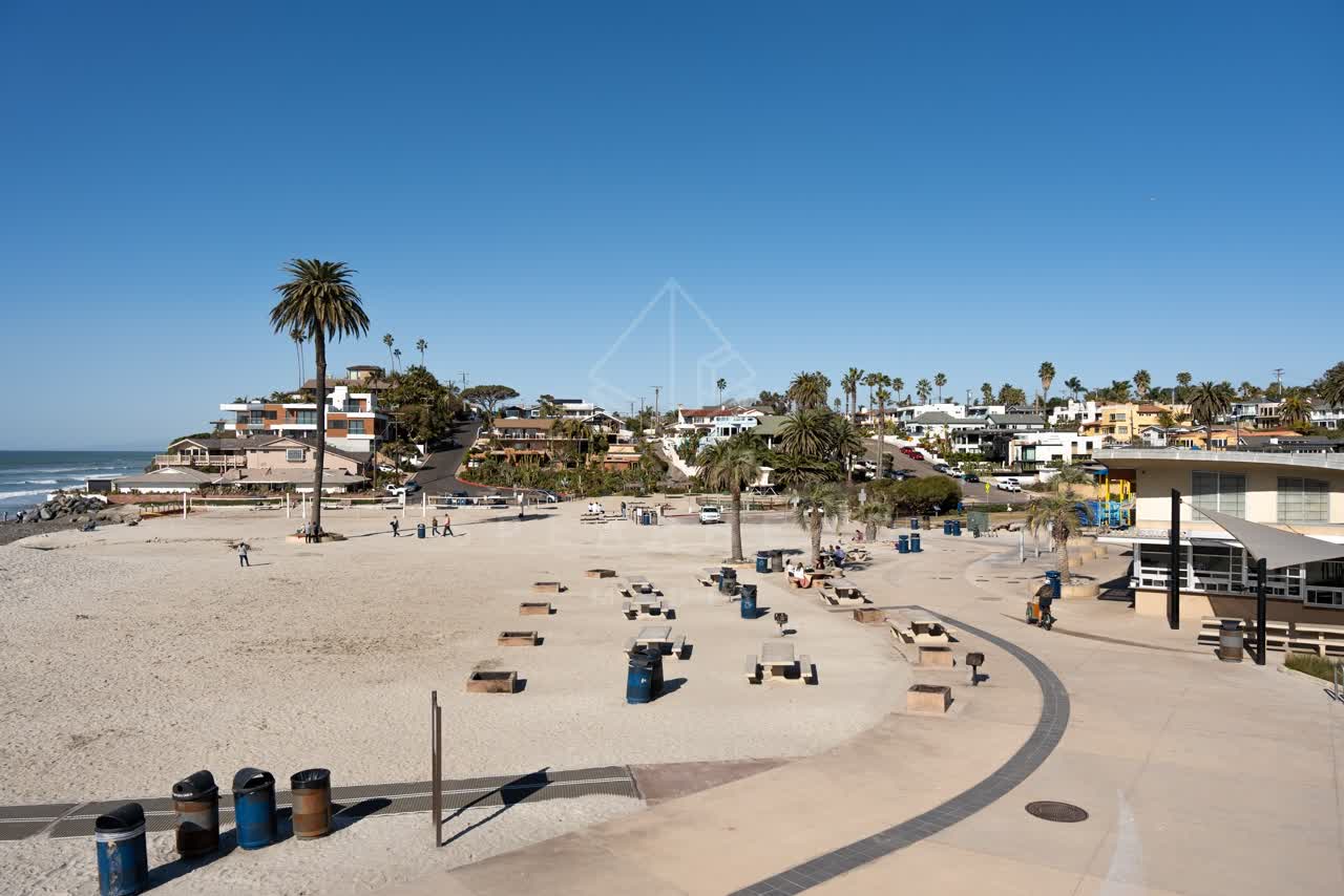 Elevated view of the beach, palm trees and the ocean at Moonlight Beach, with people walking.