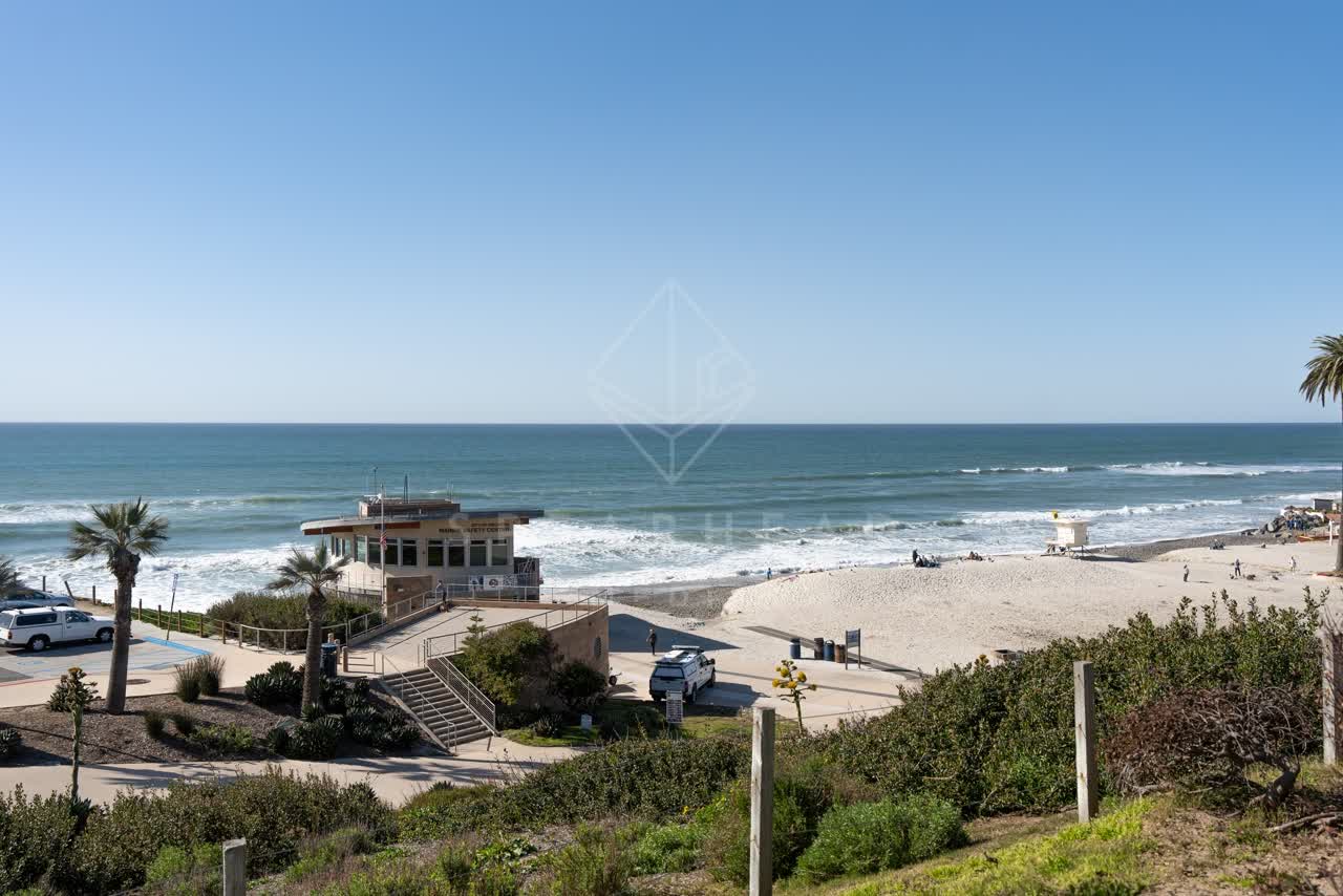 Elevated view of the beach, the surf and palm trees at Moonlight Beach, with people walking.