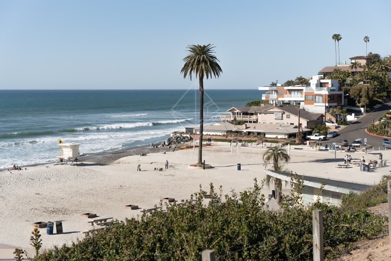 Elevated view of the beach, the surf and palm trees at Moonlight Beach, with people walking.