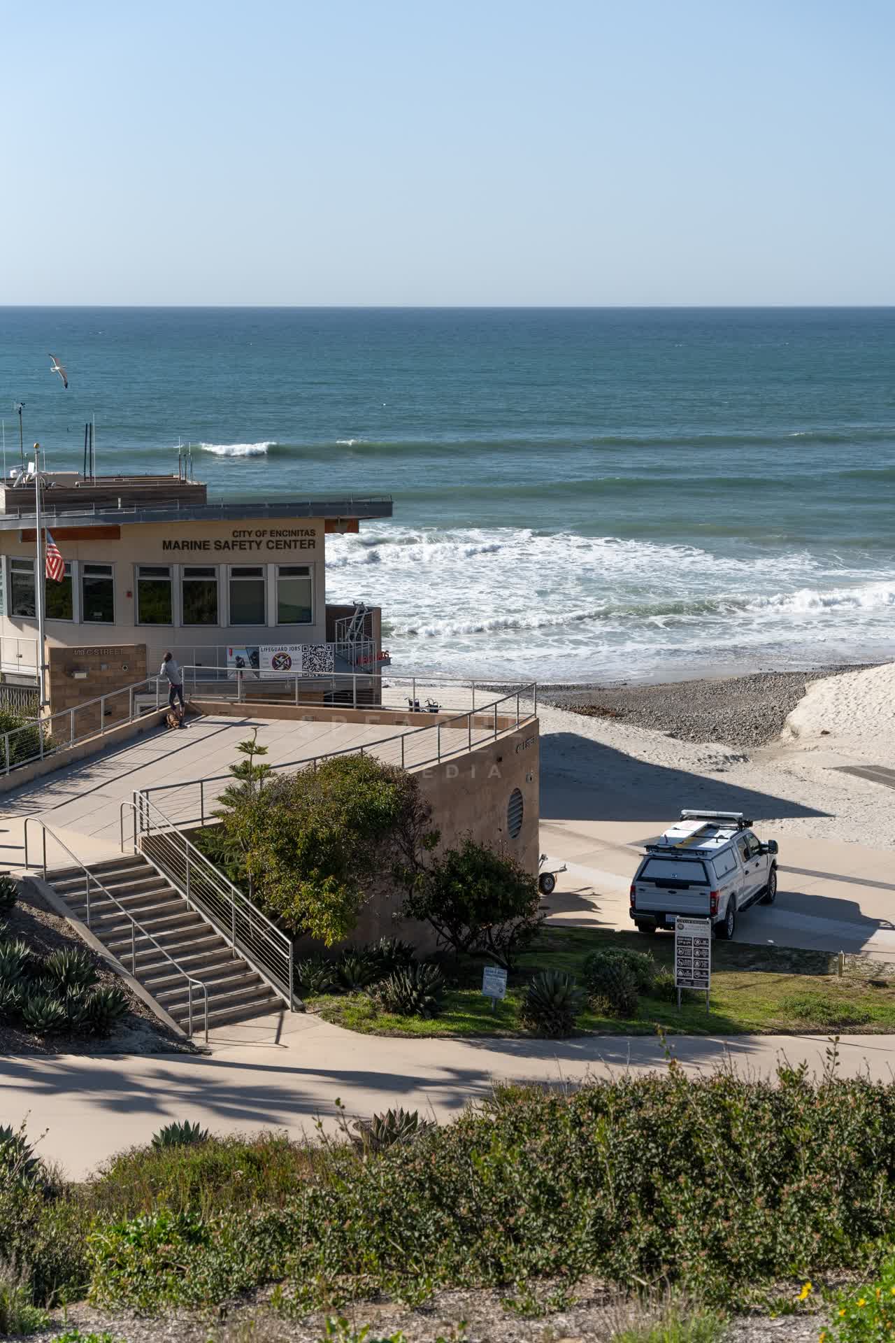 Elevated view of the beach, the surf and the ocean at Moonlight Beach, with people walking.