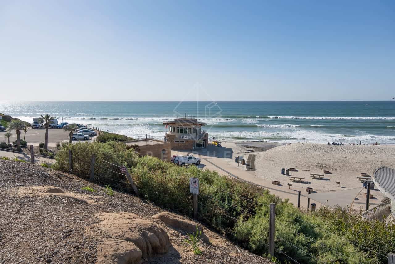 Elevated view of the beach, the surf and palm trees at Moonlight Beach, with people walking.