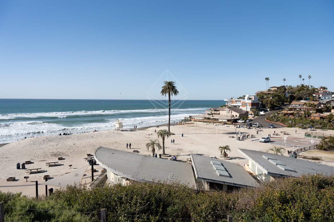 Elevated view of the beach, the surf and palm trees at Moonlight Beach, with people walking.