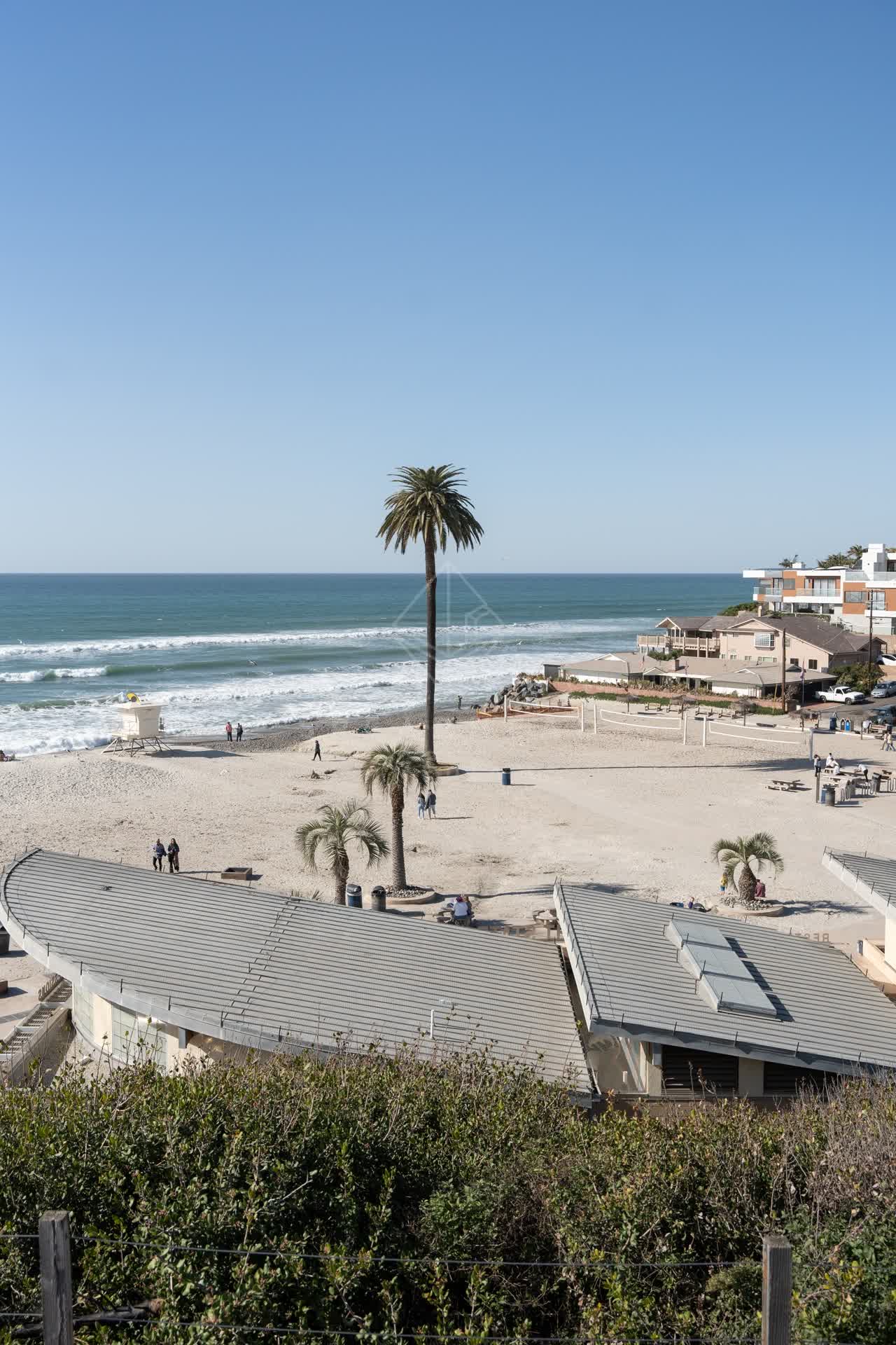 Elevated view of the beach, the surf and palm trees at Moonlight Beach, with people walking.