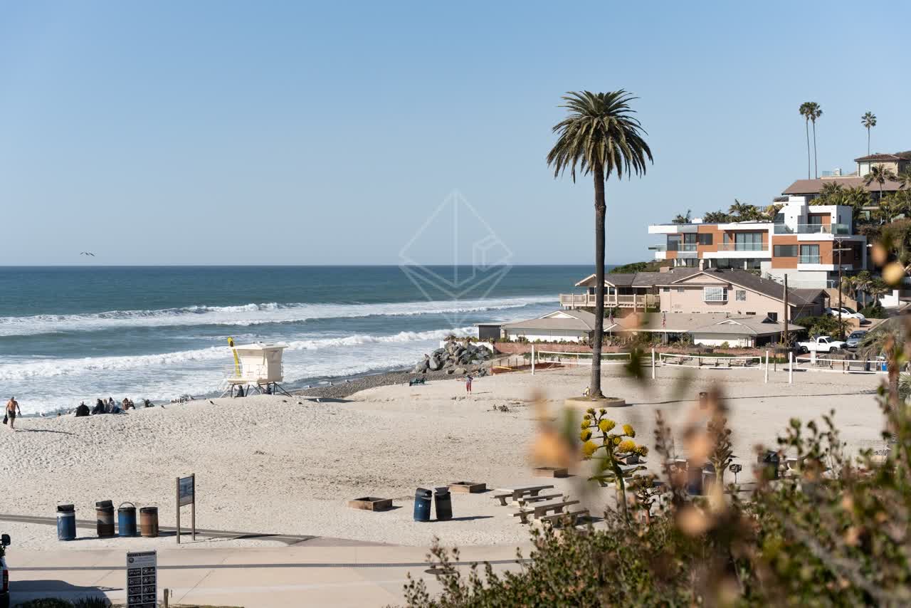 Elevated view of the beach, the surf and palm trees at Moonlight Beach, with people walking.
