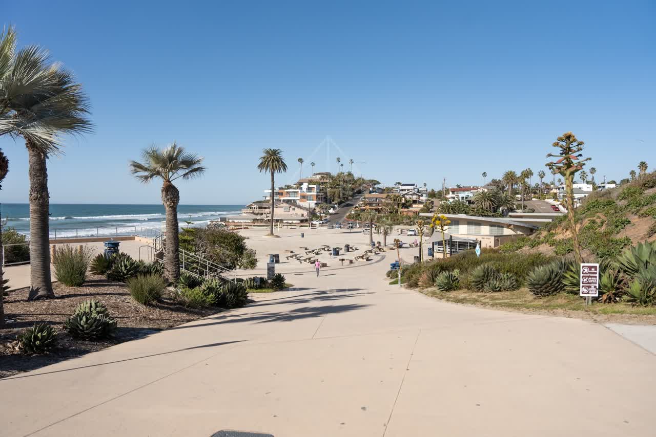 Elevated view of the beach, the surf and palm trees at Moonlight Beach, with people walking.