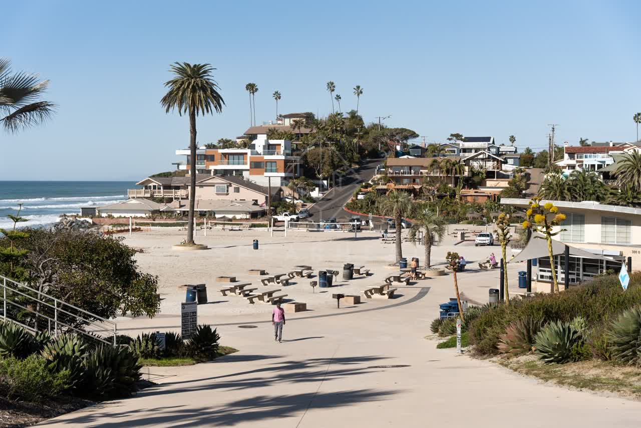 Elevated view of the beach, palm trees and the ocean at Moonlight Beach, with people walking.