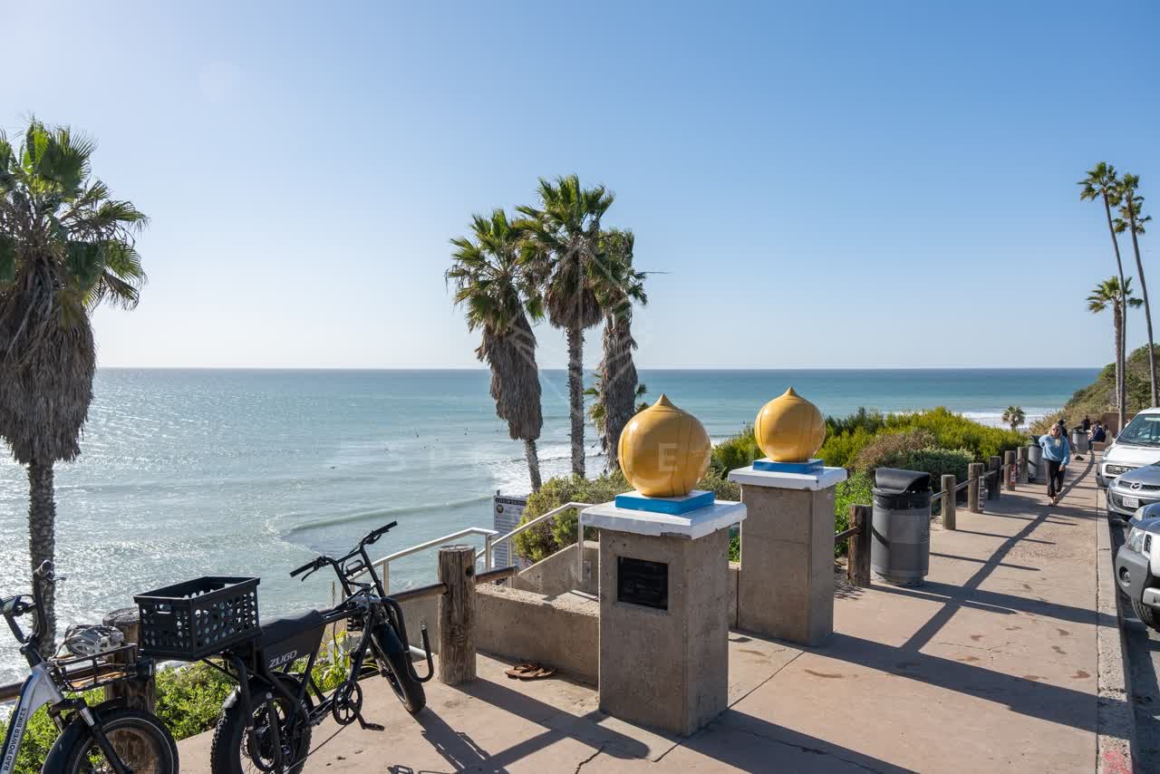 Elevated view of the cliffs, the surf and palm trees at Swamis, with people walking.