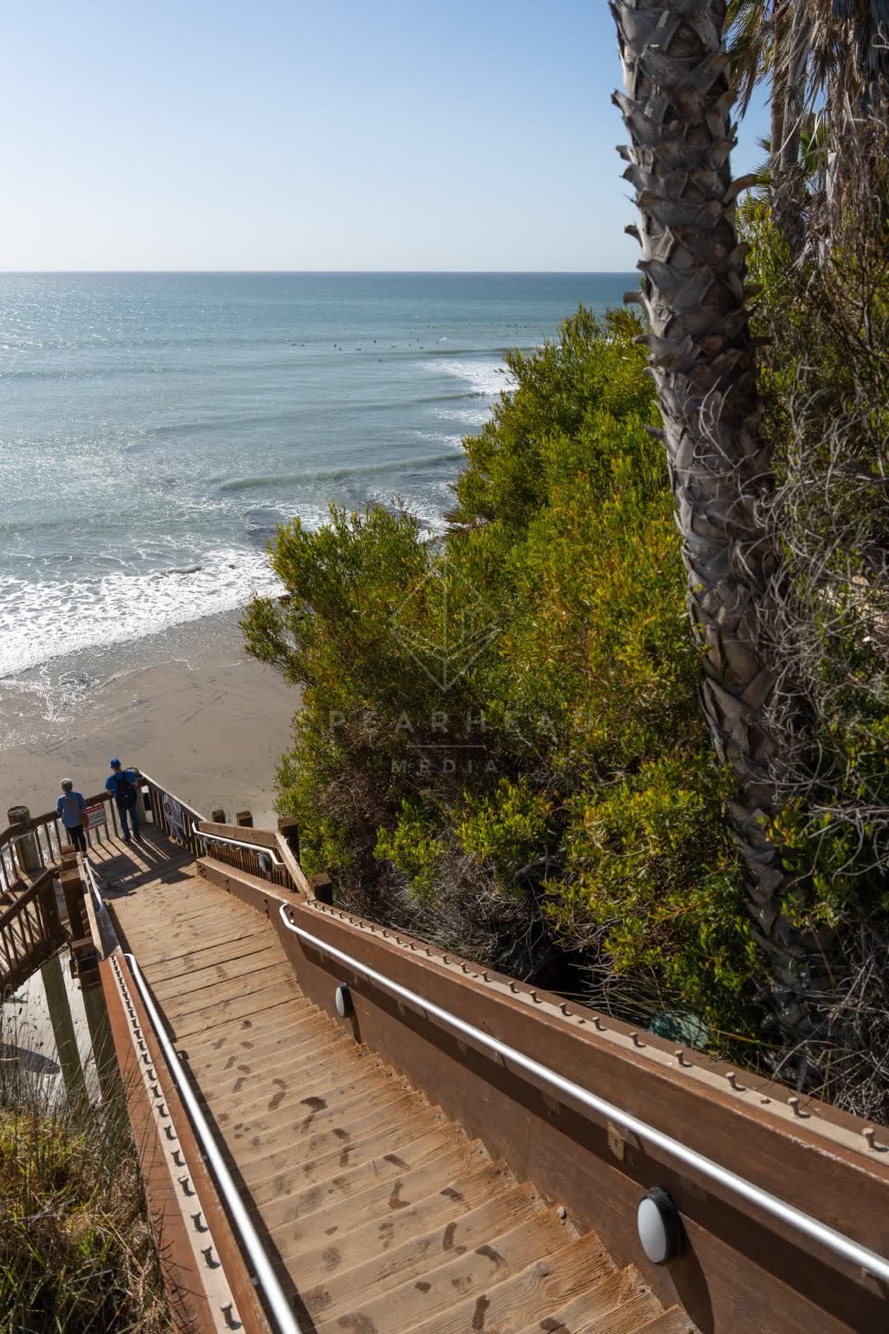 Elevated view of the cliffs, the surf and palm trees at Swamis, with people walking.