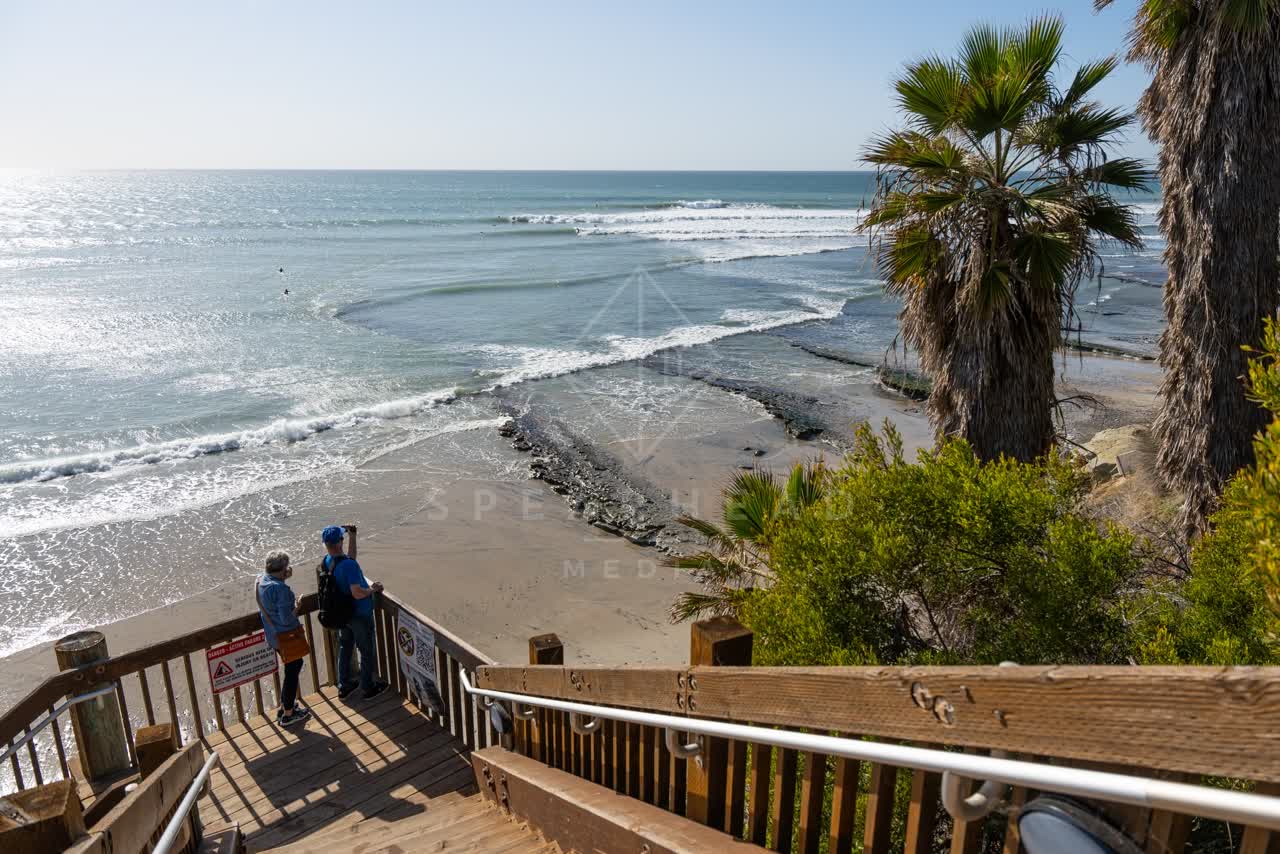 Elevated view of the beach, the surf and palm trees at Swamis, with people walking.