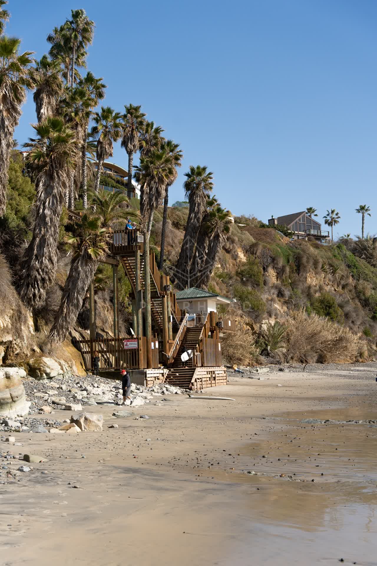 The beach, palm trees and homes at Swamis, with people walking.