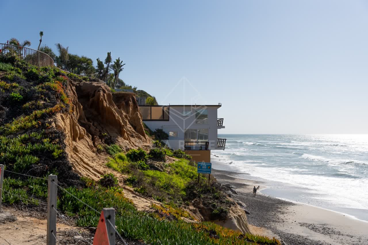 Elevated view of the cliffs, the surf and palm trees at Moonlight Beach, with people walking.