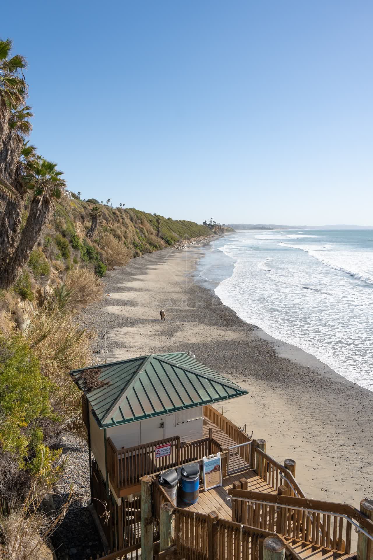 Elevated view of the beach, the surf and palm trees at Swamis, with people walking.