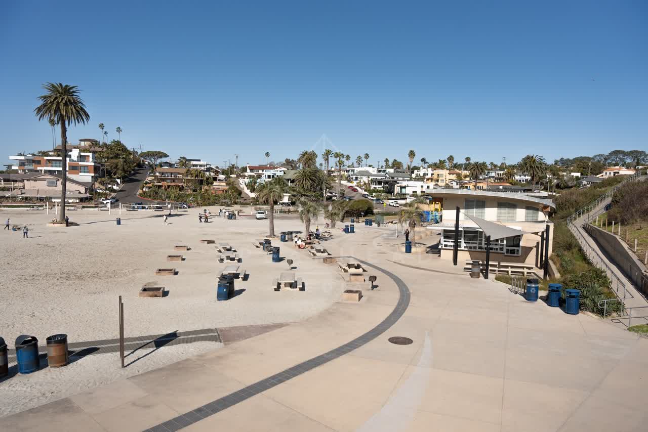 Elevated view of the beach, palm trees and the ocean at Moonlight Beach, with people walking.
