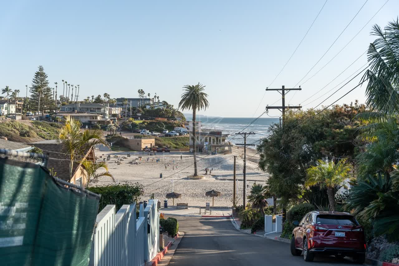 Elevated view of a residential street, palm trees and the ocean at Moonlight Beach, with people walking.