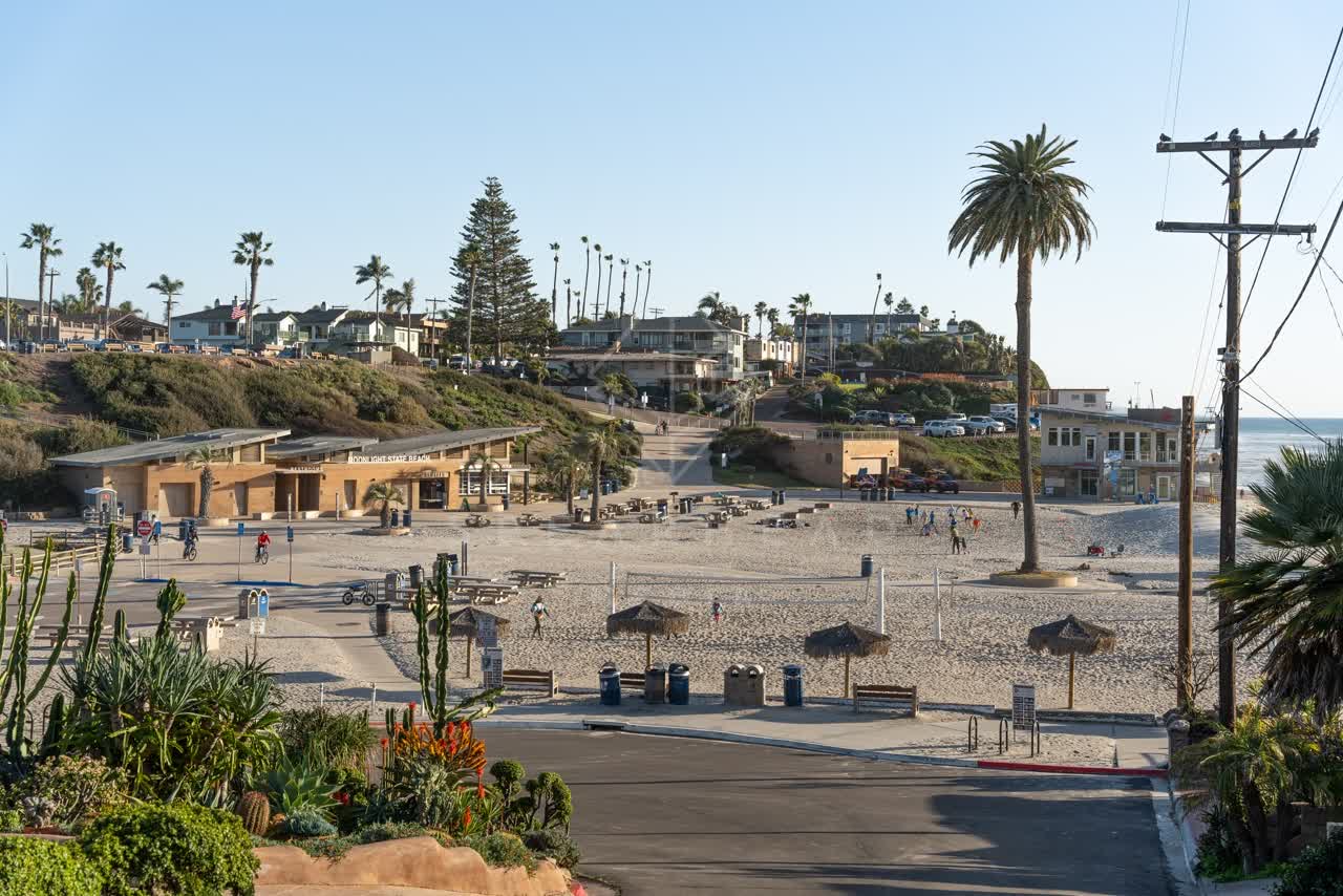 Elevated view of the beach, palm trees and the ocean at Moonlight Beach, with people walking.