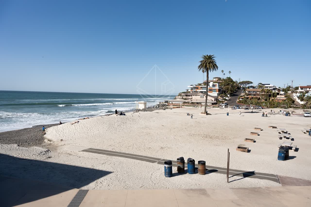 Elevated view of the beach, the surf and palm trees at Moonlight Beach, with people walking.