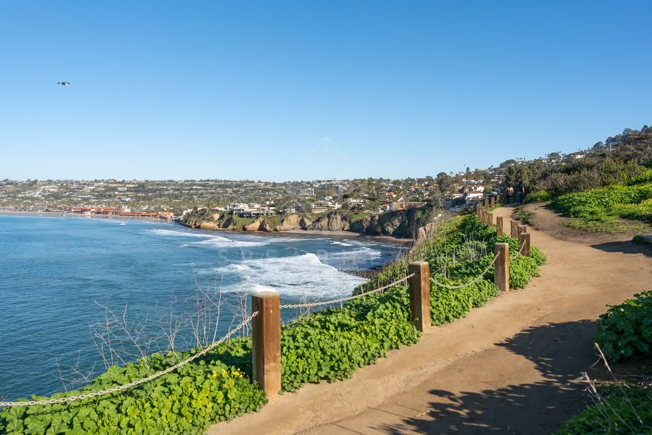 Elevated view of the cliffs, the ocean and homes at Coast Walk Trail, with people walking.