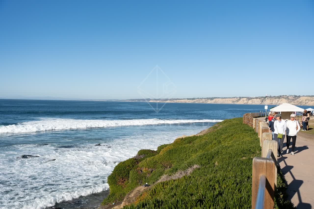 Elevated view of the cliffs, the surf and the ocean at La Jolla Cove, with people walking.