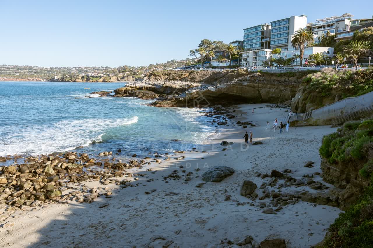 Elevated view of the beach, palm trees and the ocean at La Jolla Cove, with people walking.