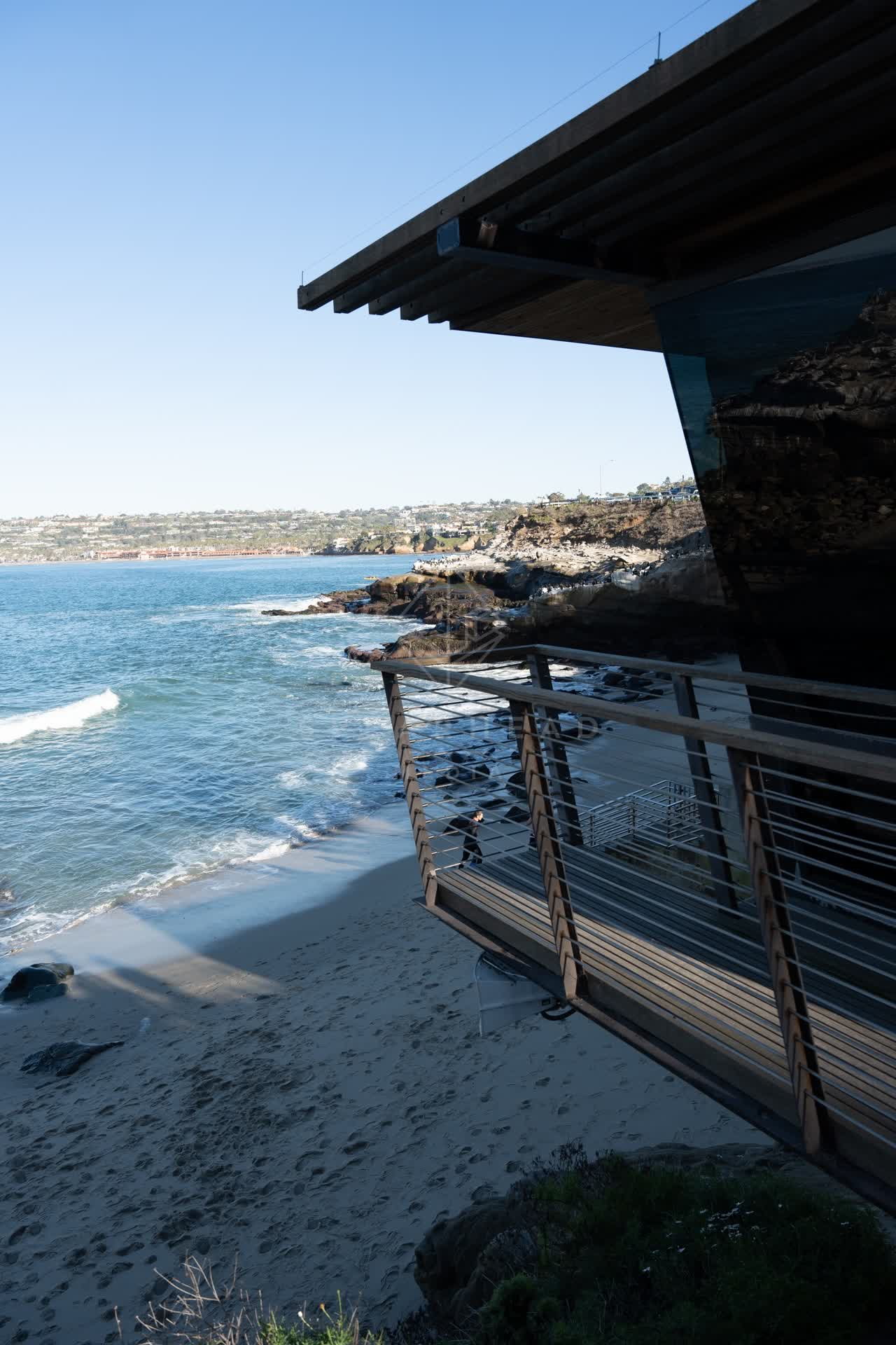 Elevated view of the cliffs, the surf and the ocean at La Jolla Cove, with people walking.