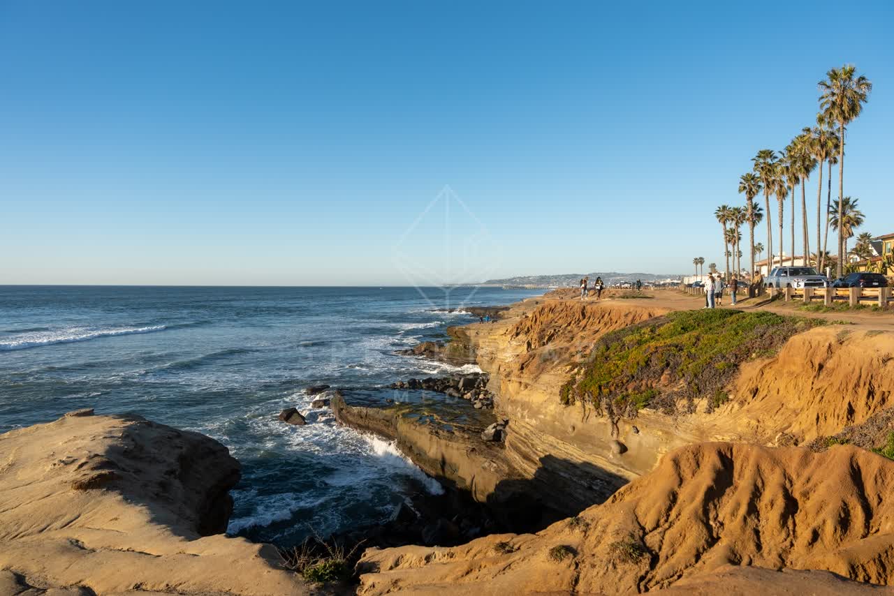 Elevated view of the cliffs, the surf and palm trees at Sunset Cliffs, with people walking.