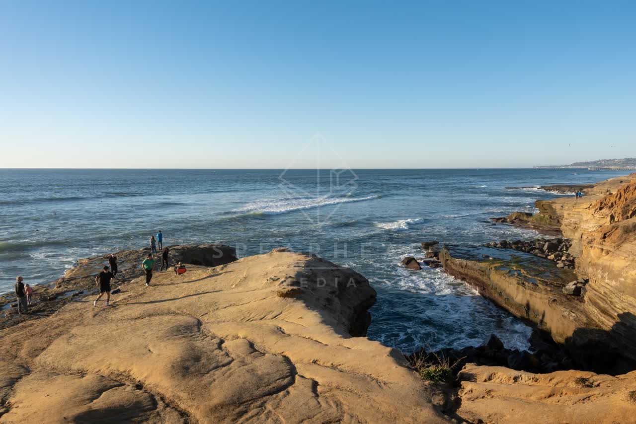 Elevated view of the cliffs, the surf and the ocean at Sunset Cliffs, with people walking.