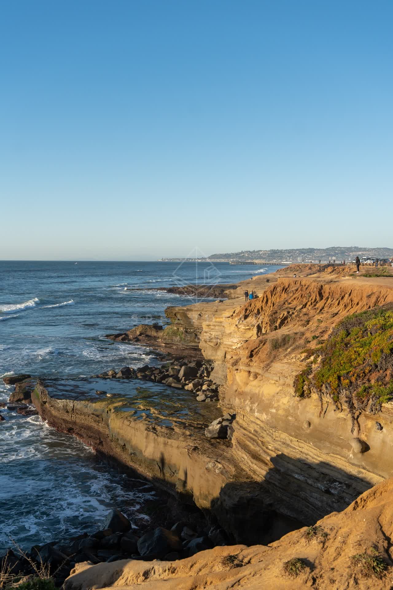 Elevated view of the cliffs, the surf and the ocean at Sunset Cliffs, with people walking.