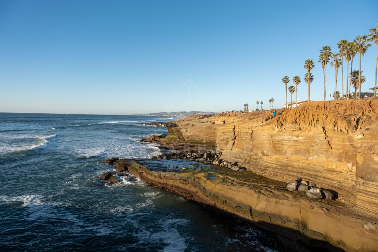 Elevated view of the cliffs, the surf and palm trees at Sunset Cliffs, with people walking.