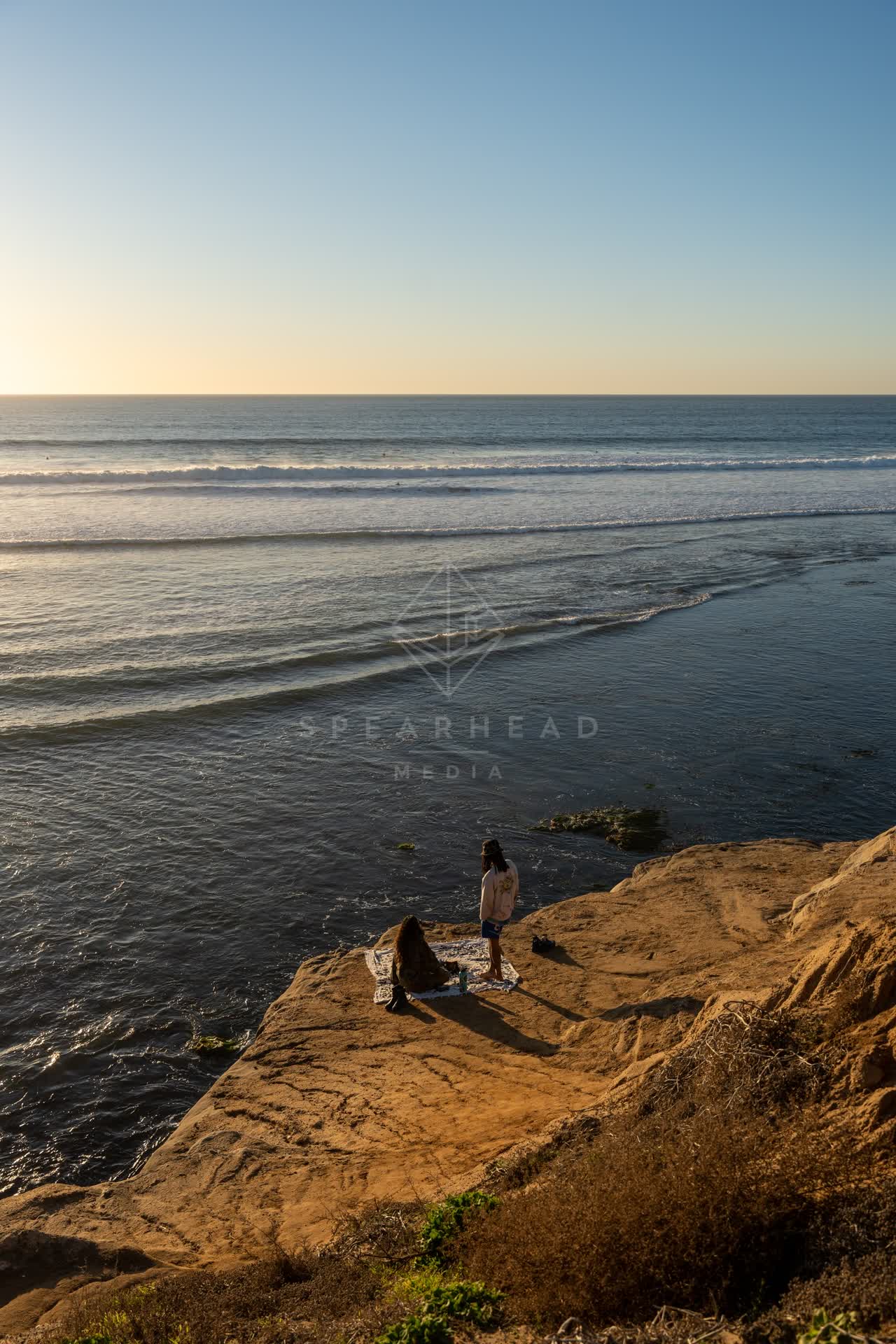 Elevated view of the cliffs, the surf and the ocean at Sunset Cliffs, with a crowd gathered.