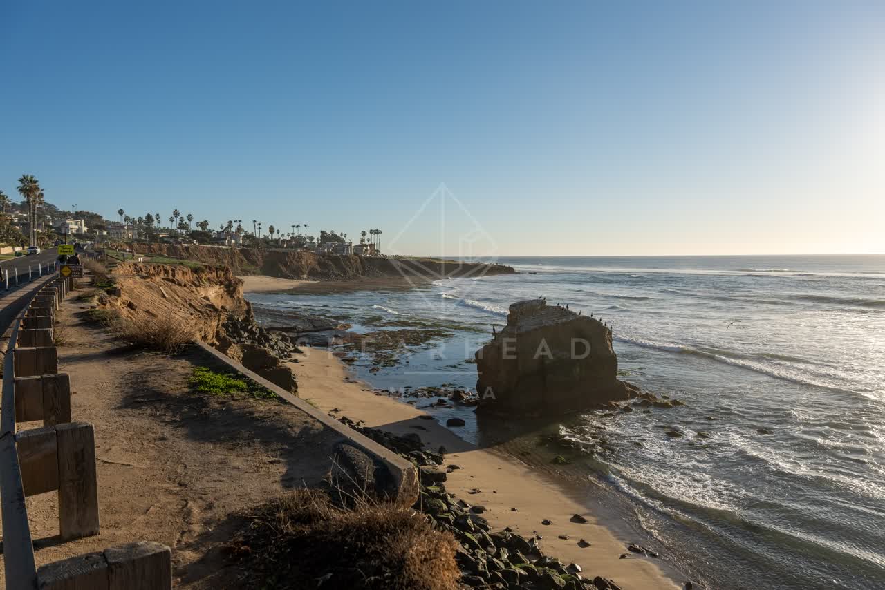 Elevated view of the cliffs, the surf and palm trees at Sunset Cliffs, with people walking.